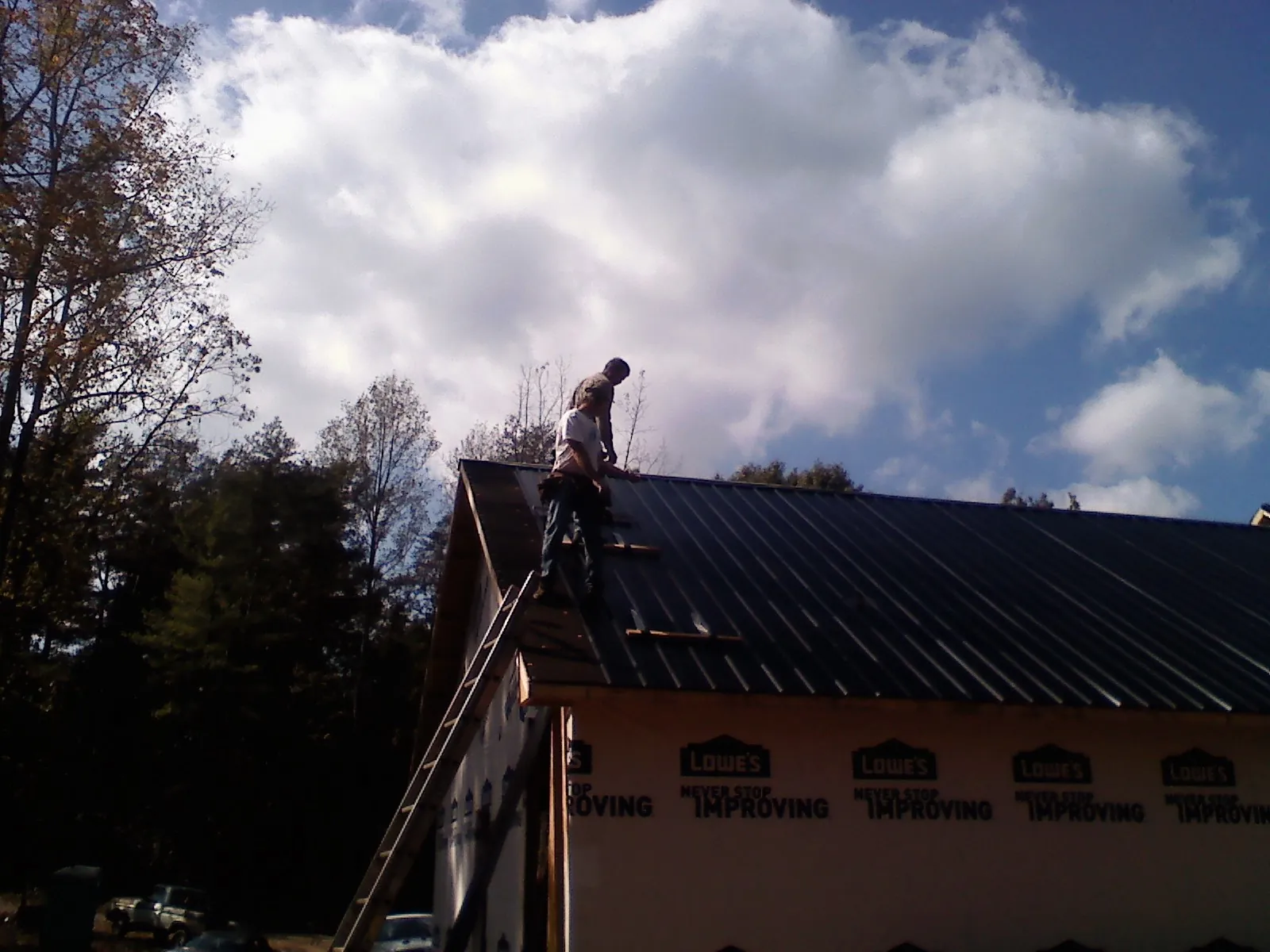 Roofer fastening dark metal panels high against a cloudy sky, from a Roof Inspection job in Charlestown